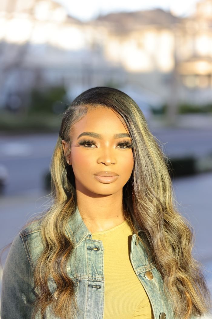 Elegant young woman in sunlight, wearing a denim jacket, with a modern hairstyle.
